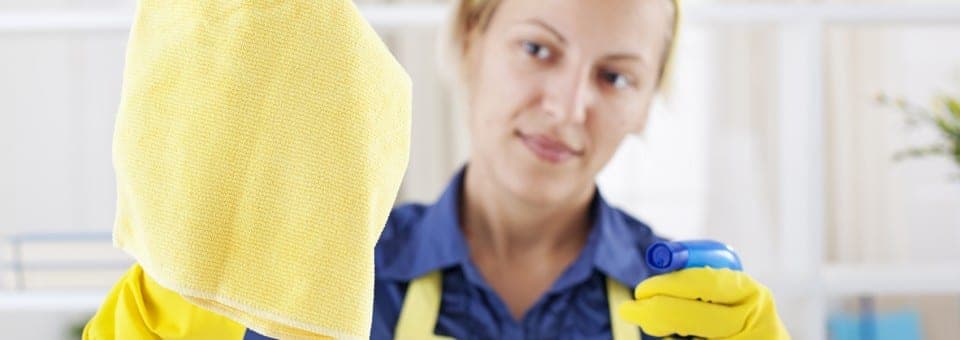 A cleaner in yellow gloves polishing a window with a microfiber cloth